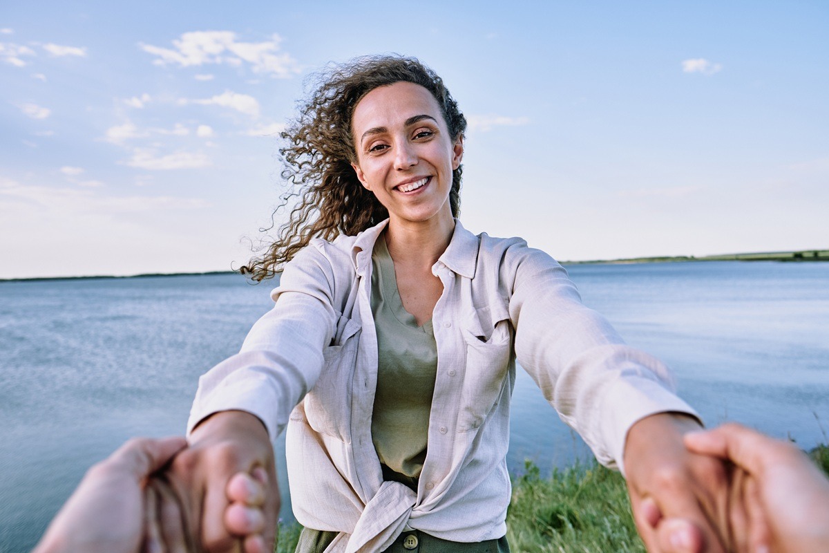Happy young female with toothy smile while holding someone's hands during reset by seaside