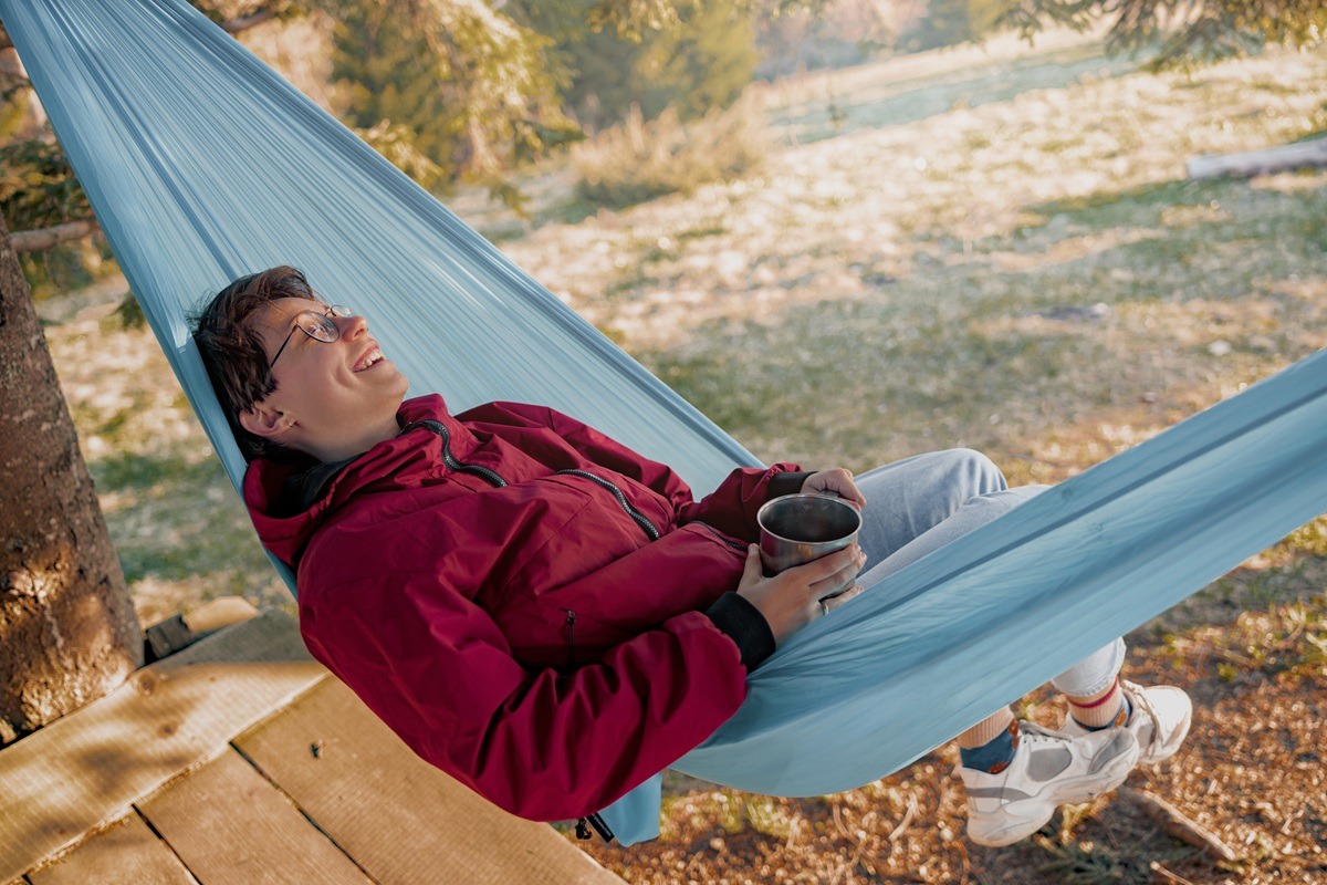 Happy cheerful woman in glasses lying in hammock. laughing and holding cup of coffee. 