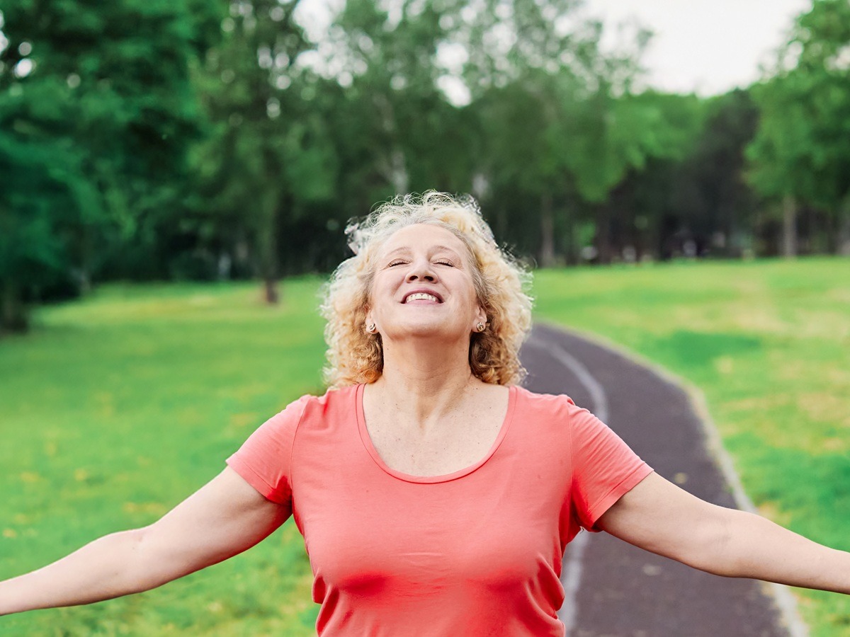 Happy active mature middle aged woman walking, running, daydreaming, meditating and relaxing in park outdoors