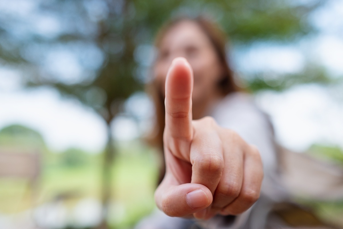 Blurred image of a woman touching or pointing finger at the camera.