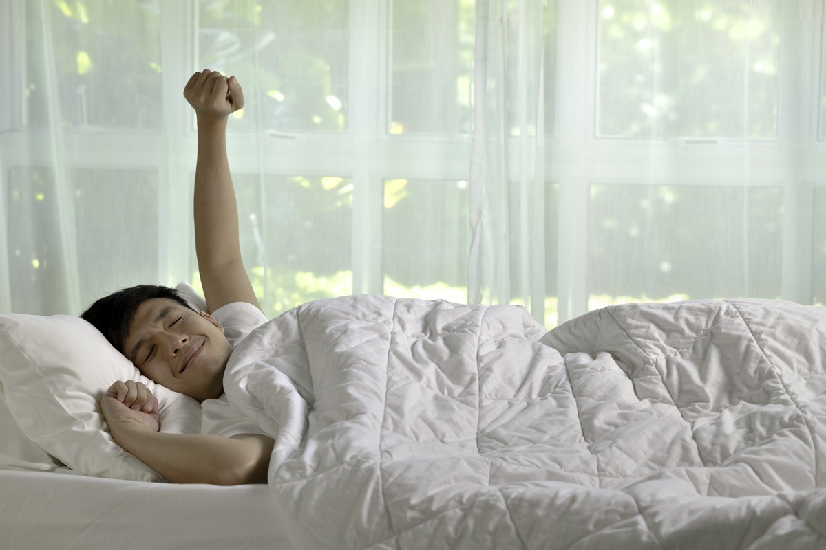 Asian man stretching in bed after wake up in the morning