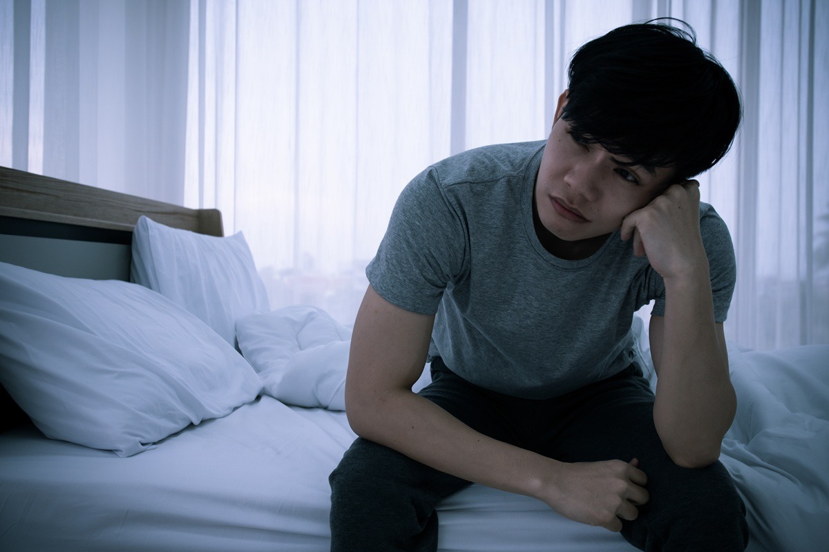 Stressed Asian young man sitting alone on bed. 