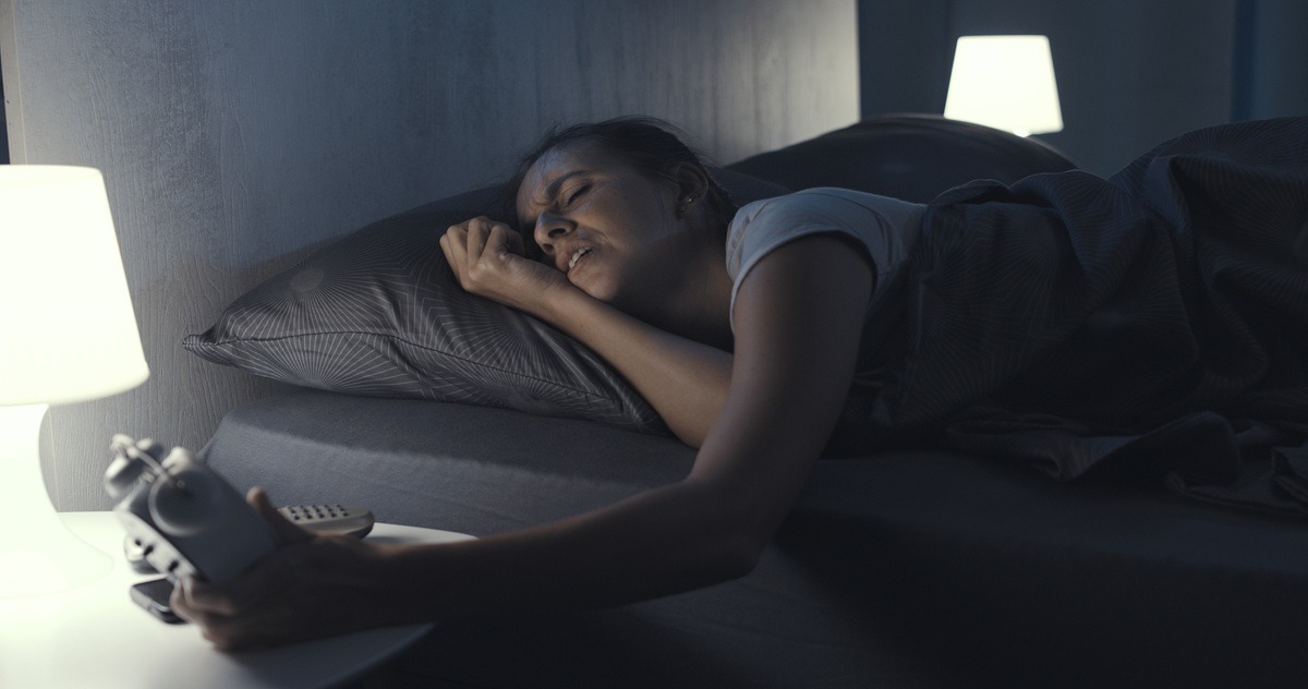 Upset woman lying in bed and checking the time on her alarm clock, she is suffering from insomnia