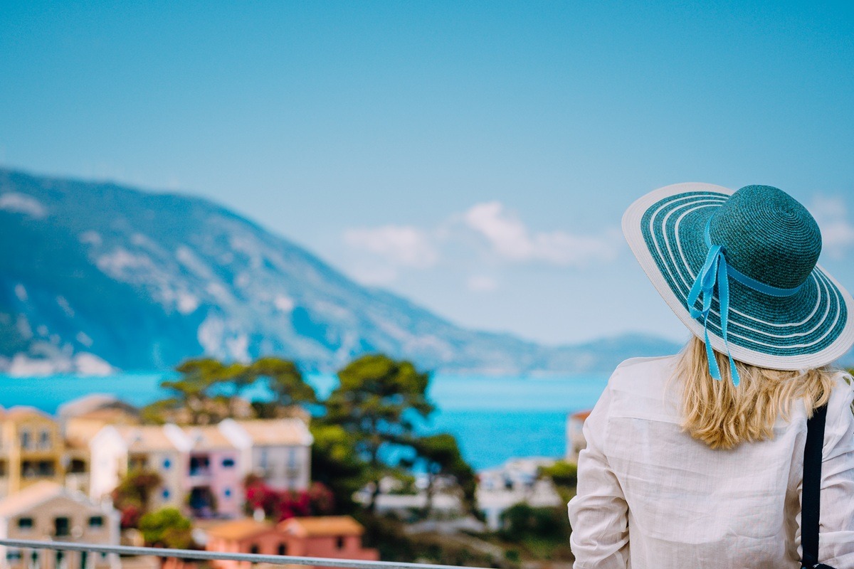 A tourist woman wearing a blue sunhat and white clothes admiring a view of colorful tranquil village Assos on sunny day. A tourist woman wearing a blue sunhat and white clothes admiring a view of colorful tranquil village Assos on sunny day.
