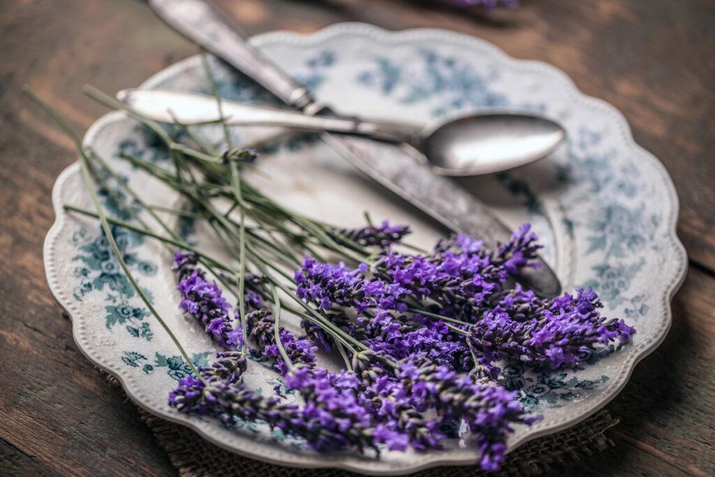 Close-up of lavender flowers on a plate with a spoon, resting on a textured wooden table. Close-up of lavender flowers on a plate with a spoon, resting on a textured wooden table.