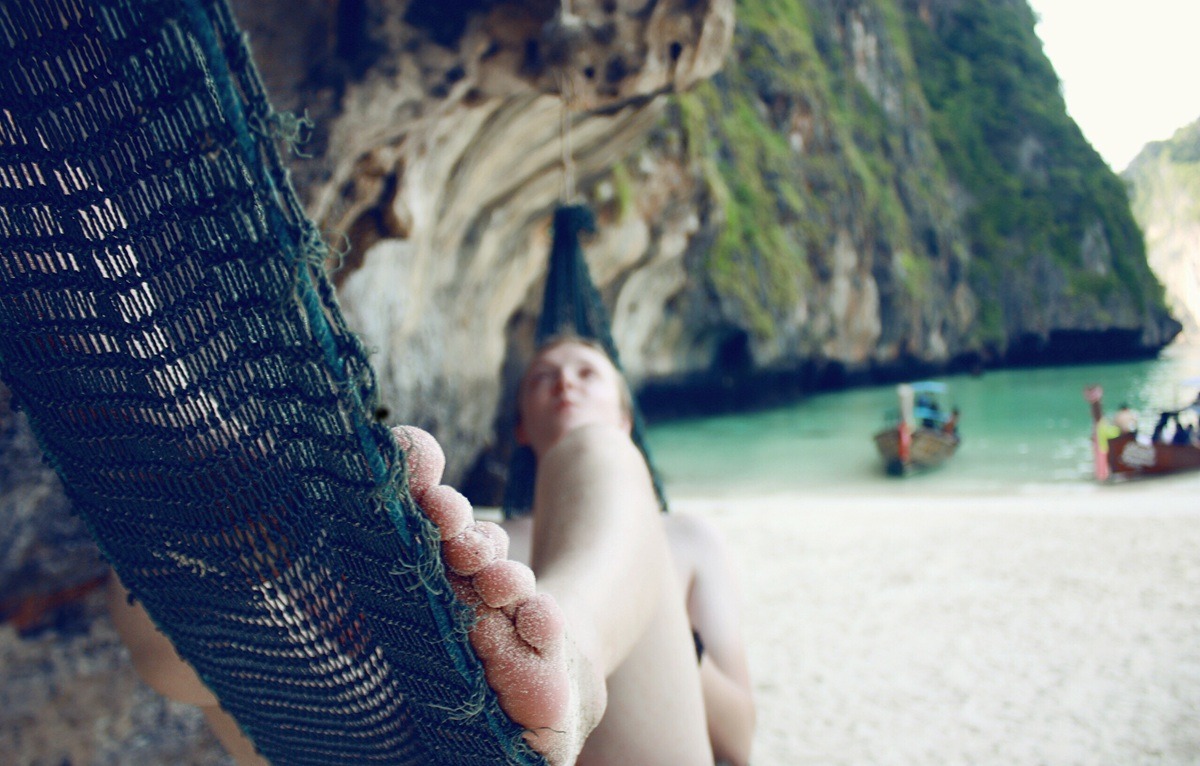 A person lying in a hammock on a white sand beach. A person lying in a hammock on a white sand beach.