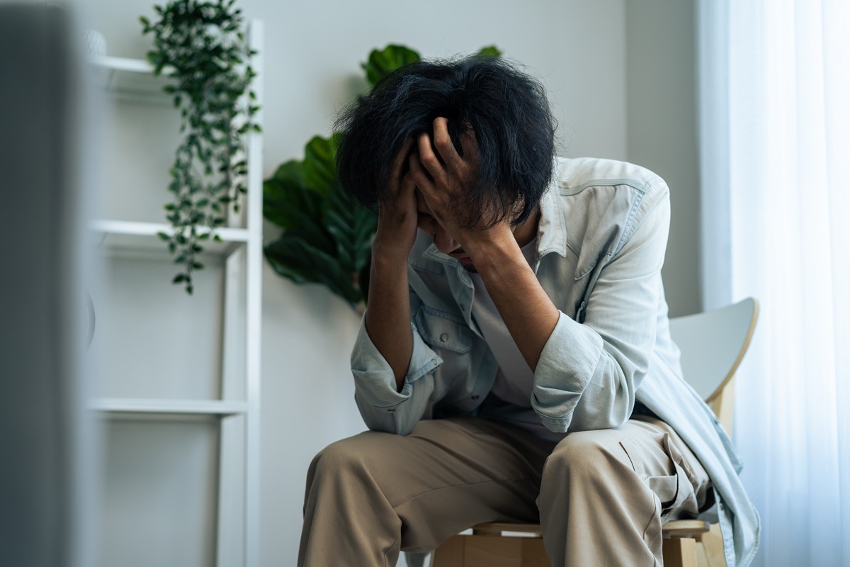 Young upset depressed man sitting alone in living room at home. 