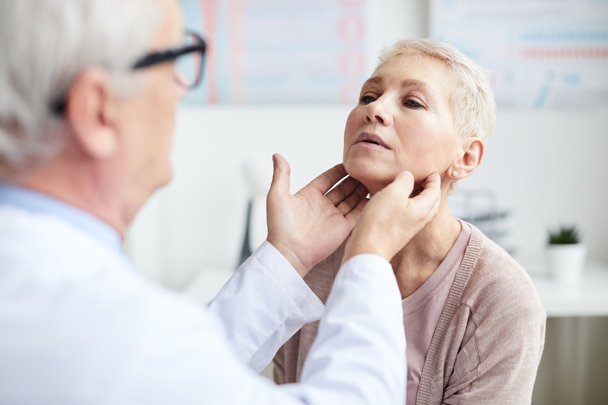 Over shoulder view of qualified doctor touching neck of mature patient.