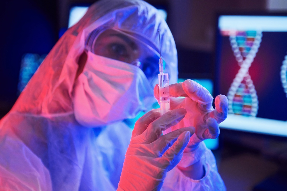 Nurse in mask and white uniform, holding syringe in neon lighted laboratory with computer and medical equipment. Nurse in mask and white uniform, holding syringe in neon lighted laboratory with computer and medical equipment.