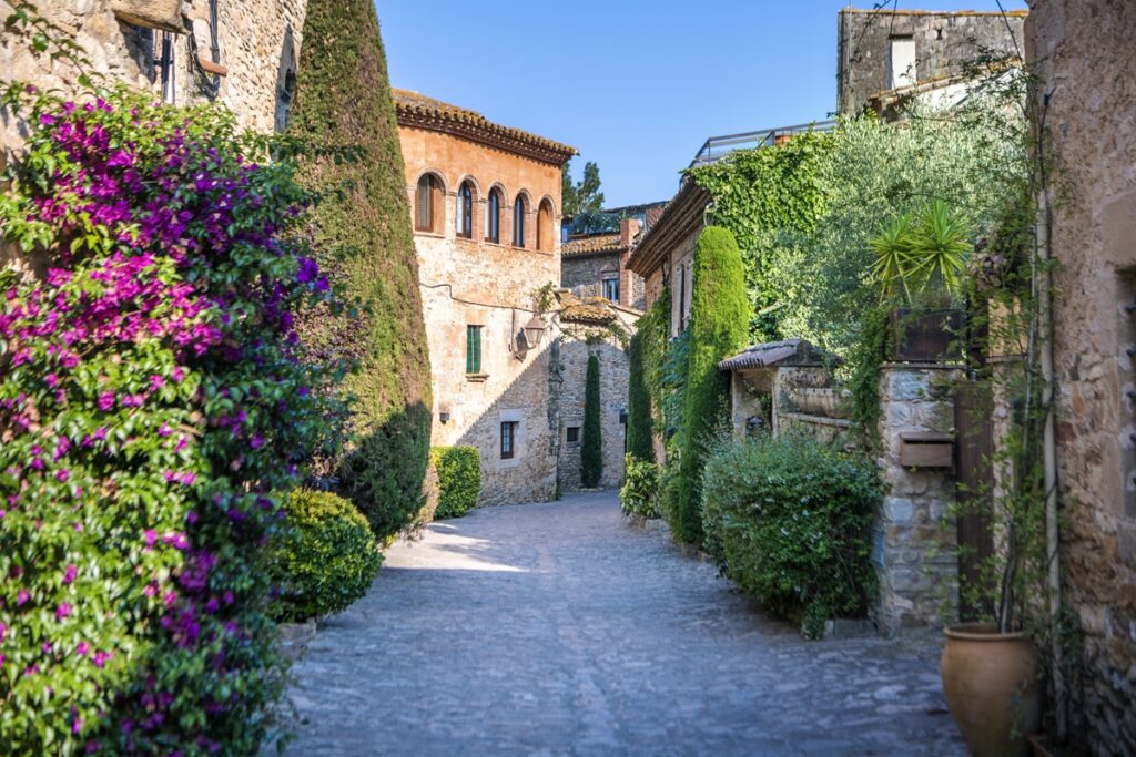 A narrow street lined with stone buildings adorned with colorful flowers, creating a charming and picturesque scene.
