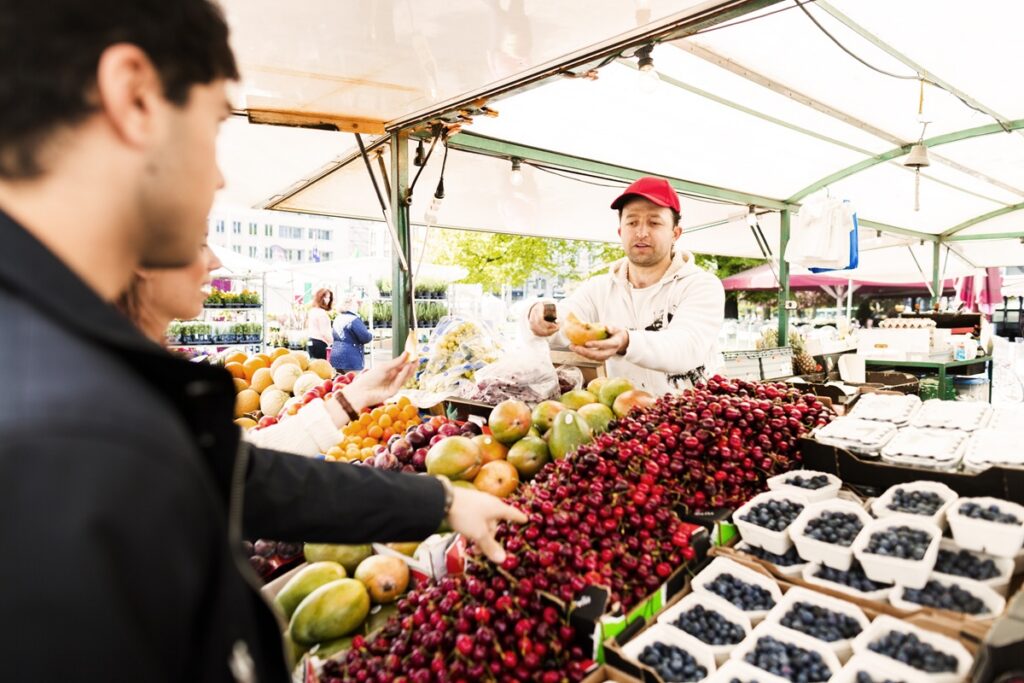 Market vendor offering vibrant fruit to customer.